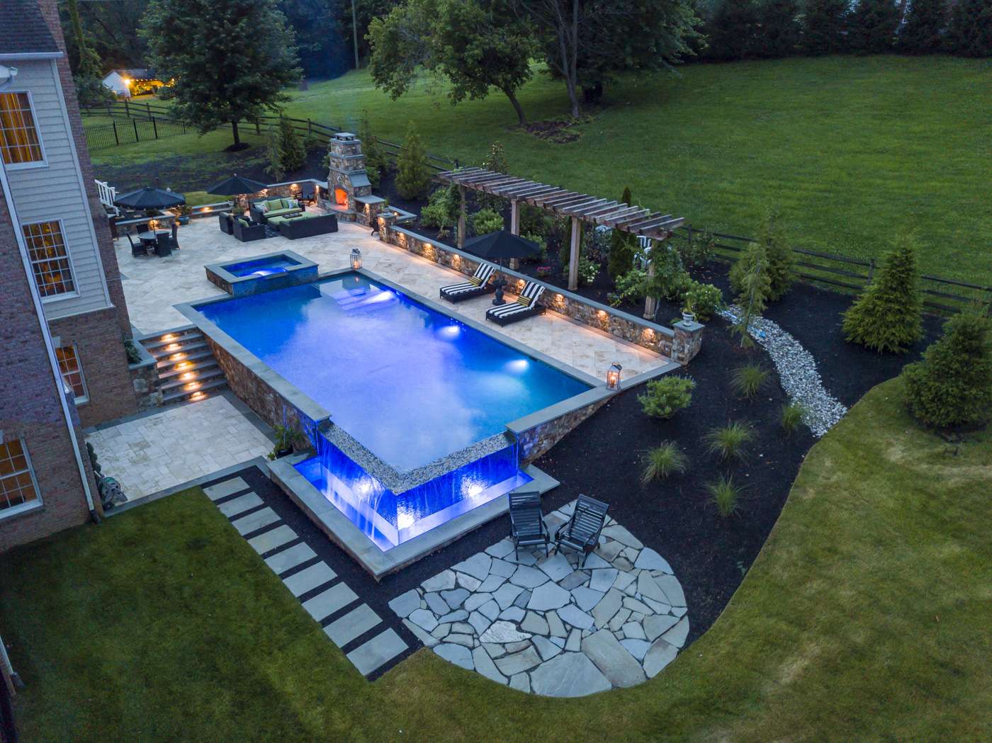 aerial view of infinity edge pool with 2 patios and outdoor fireplace