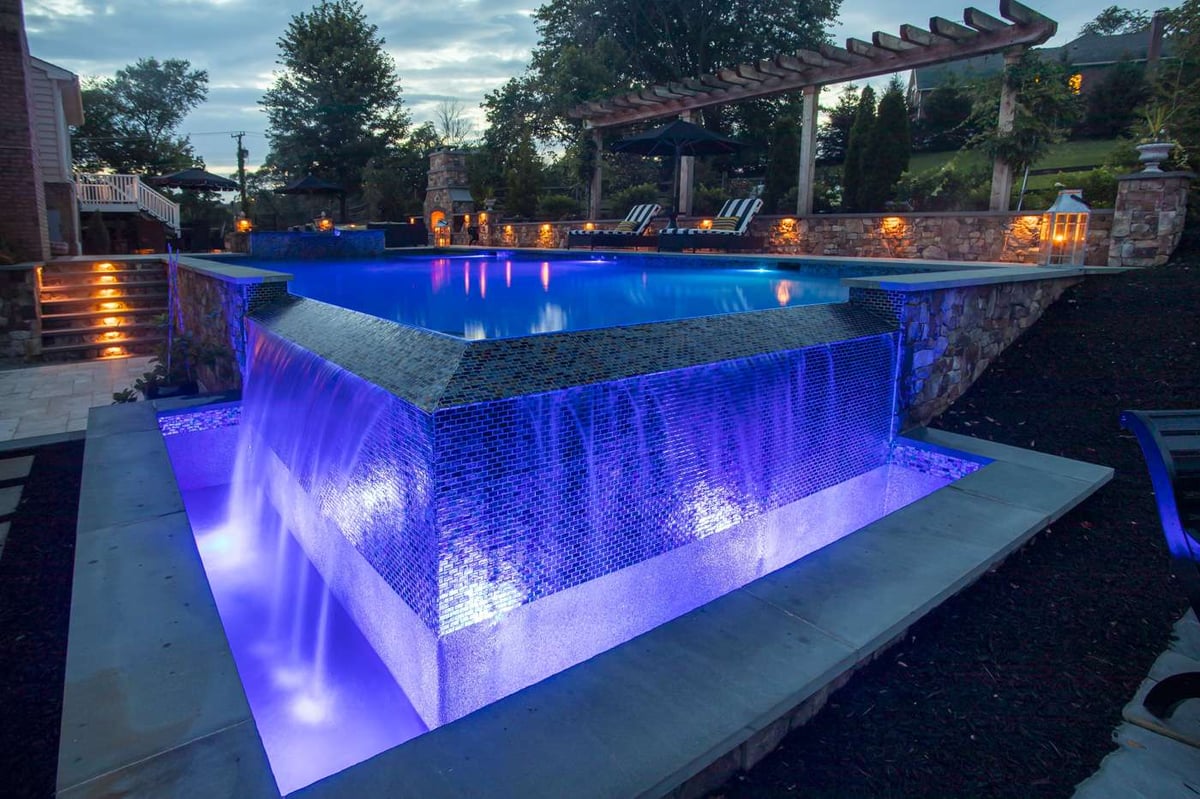 pool with lighting and hot tub with infinity edge