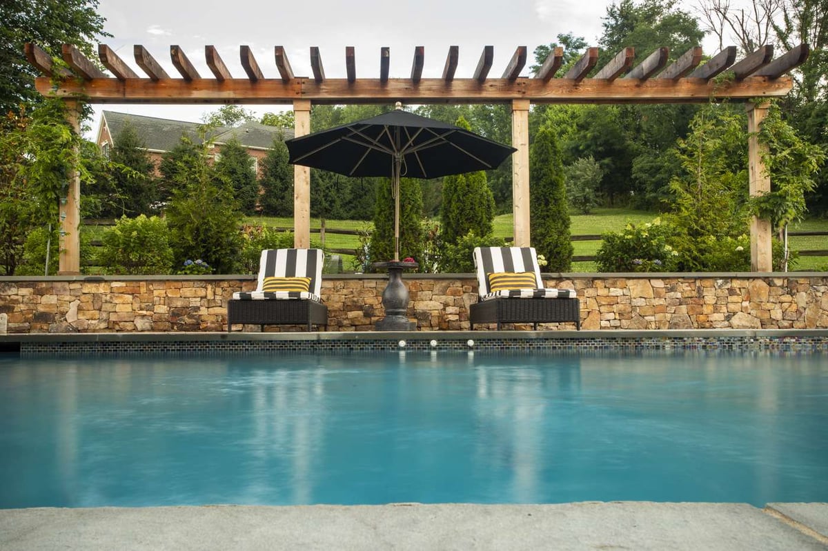 pool with stone patio and wall and pergola