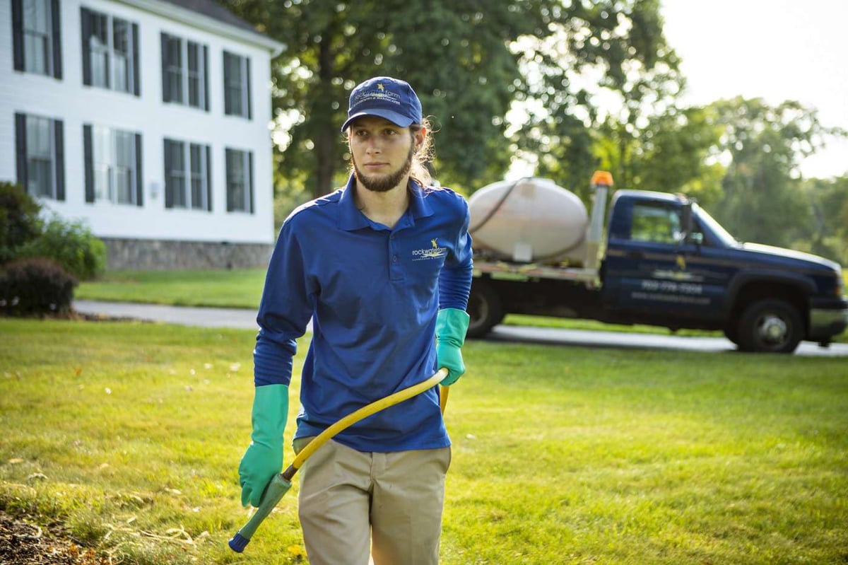 lawn care technician in uniform spraying lawn