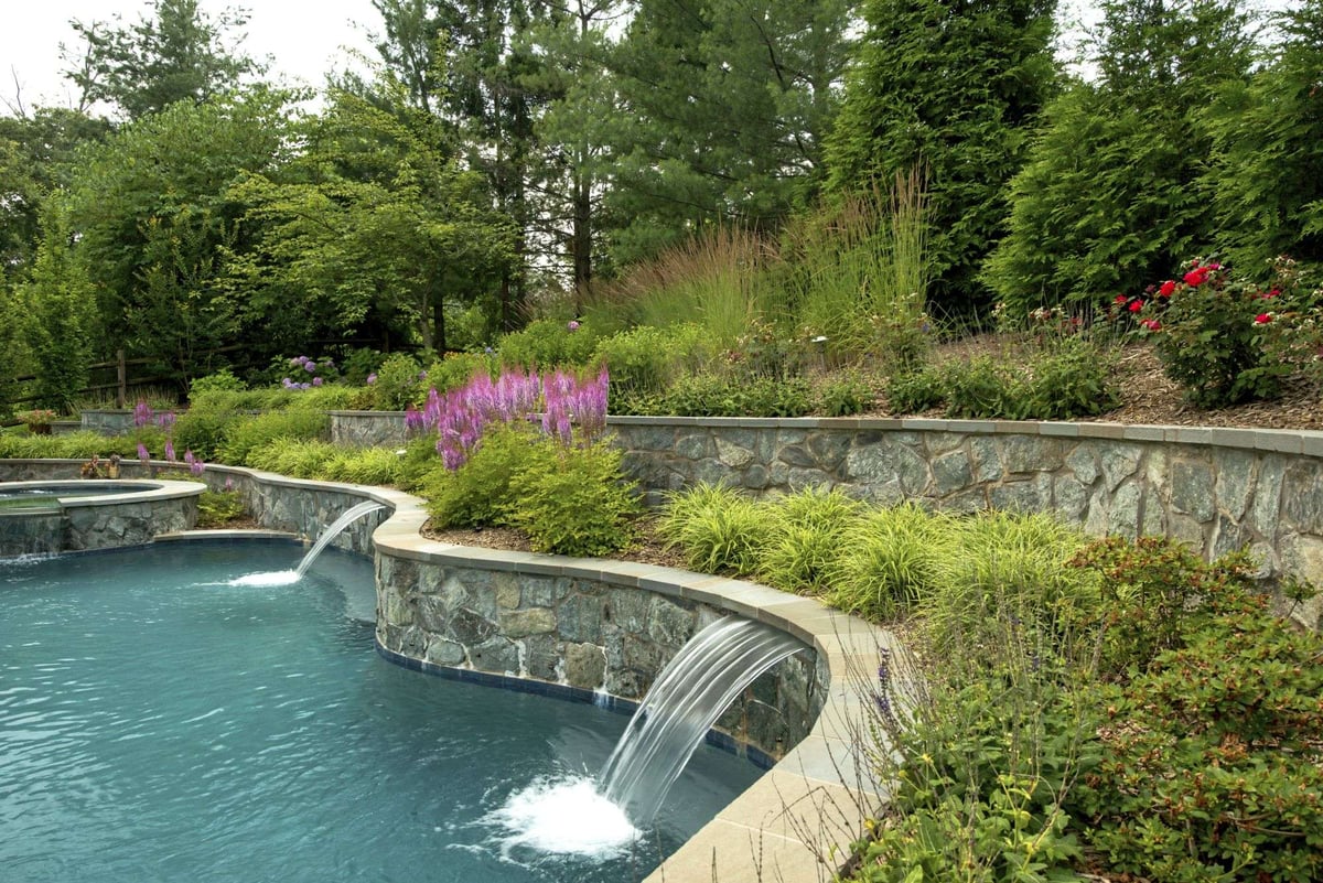 inground pool with waterfall and hot tub surrounded by plantings