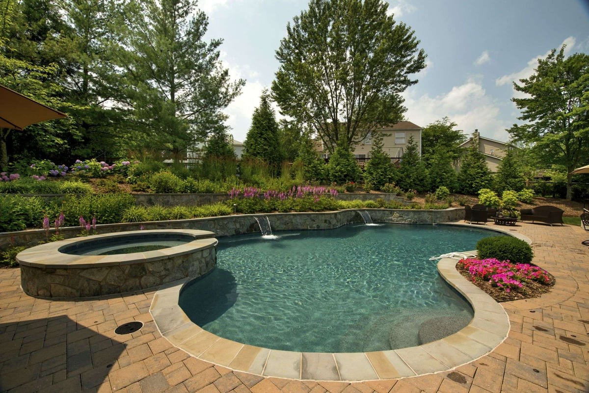paver patio surrounding pool with waterfalls and hot tub