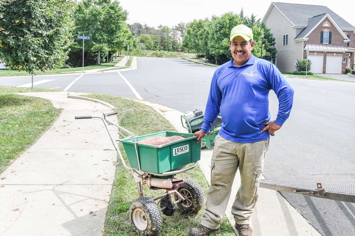 lawn care crew member with overseeding spreader and seed