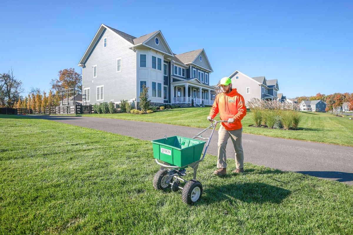 lawn care technician uses walk behind spreader to put down fertilizer