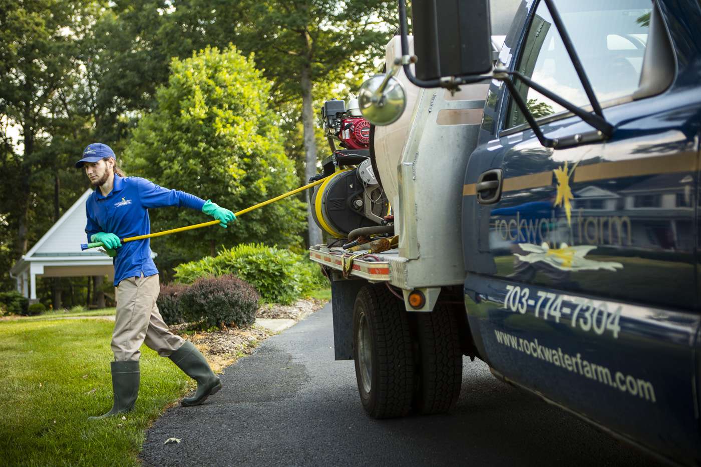landscape care crew member pulls hose from truck to apply treatment